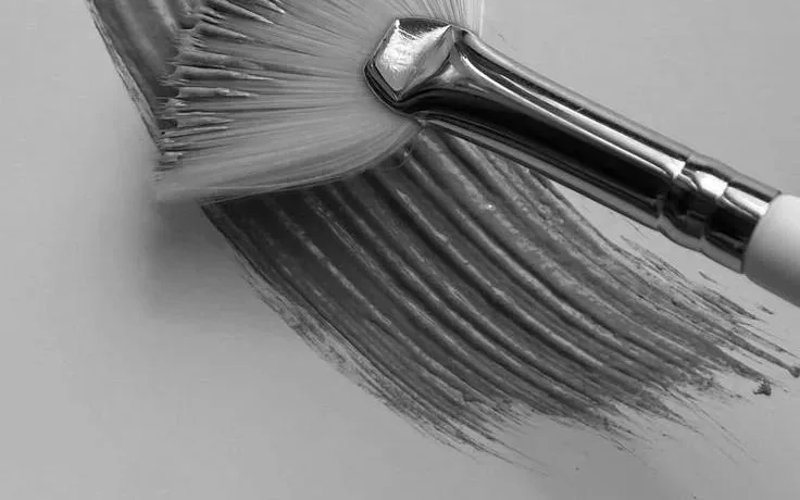 A fan brush sweeping a stroke of product across a pale background